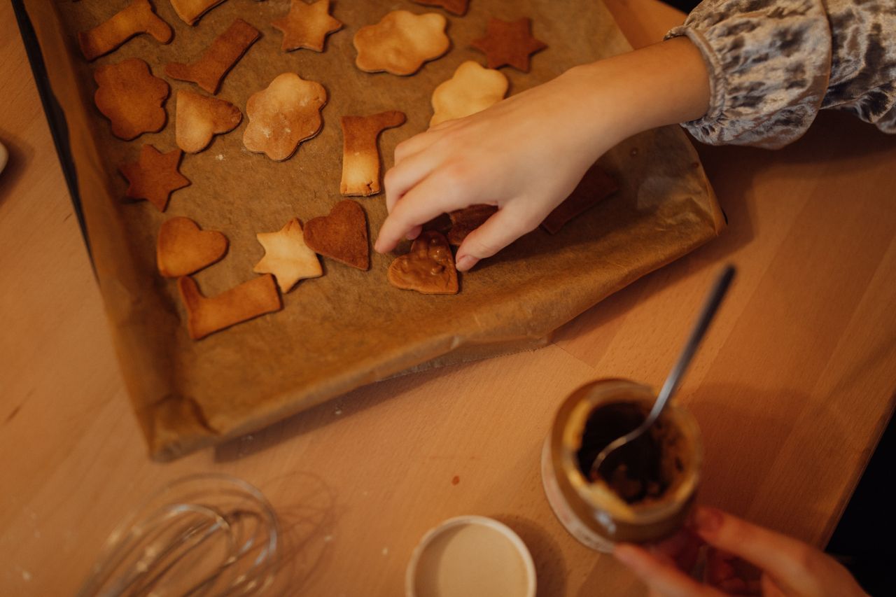 services-01 Close-up view of hands decorating star-shaped and cloud-shaped cookies on baking paper.