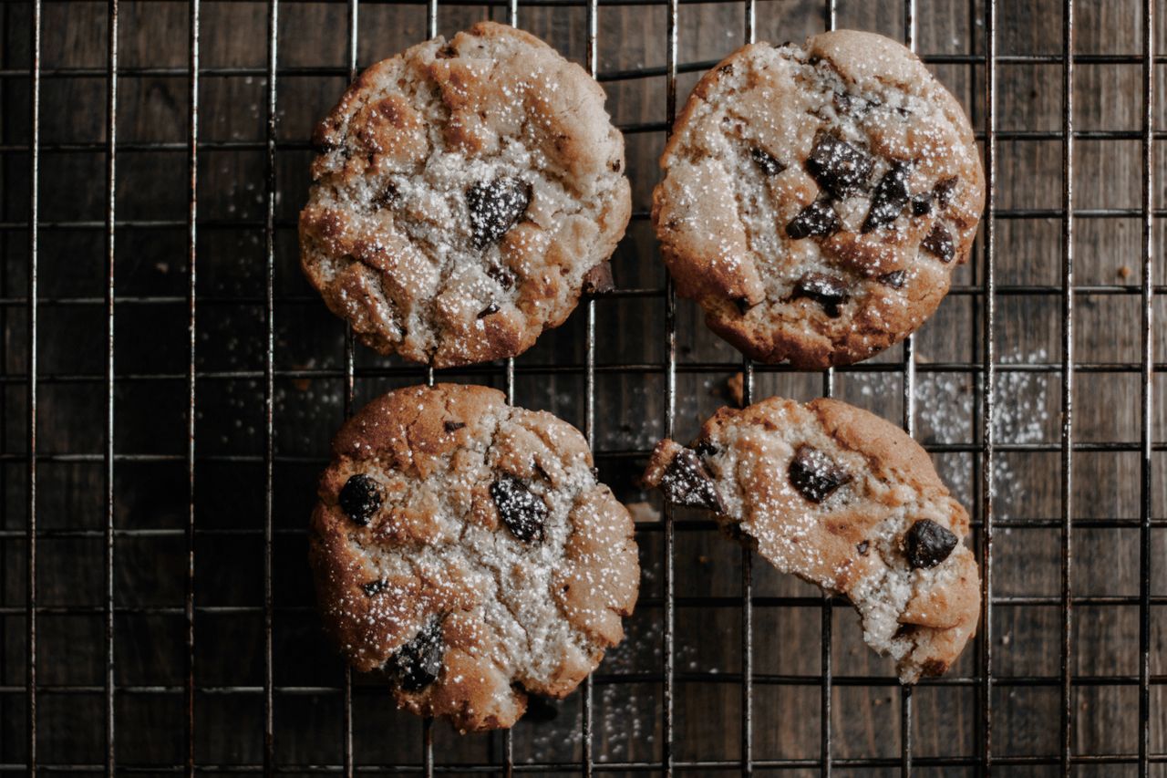 gallery-1 A tempting flatlay of freshly baked chocolate chip cookies on a cooling rack, dusted with powdered sugar.