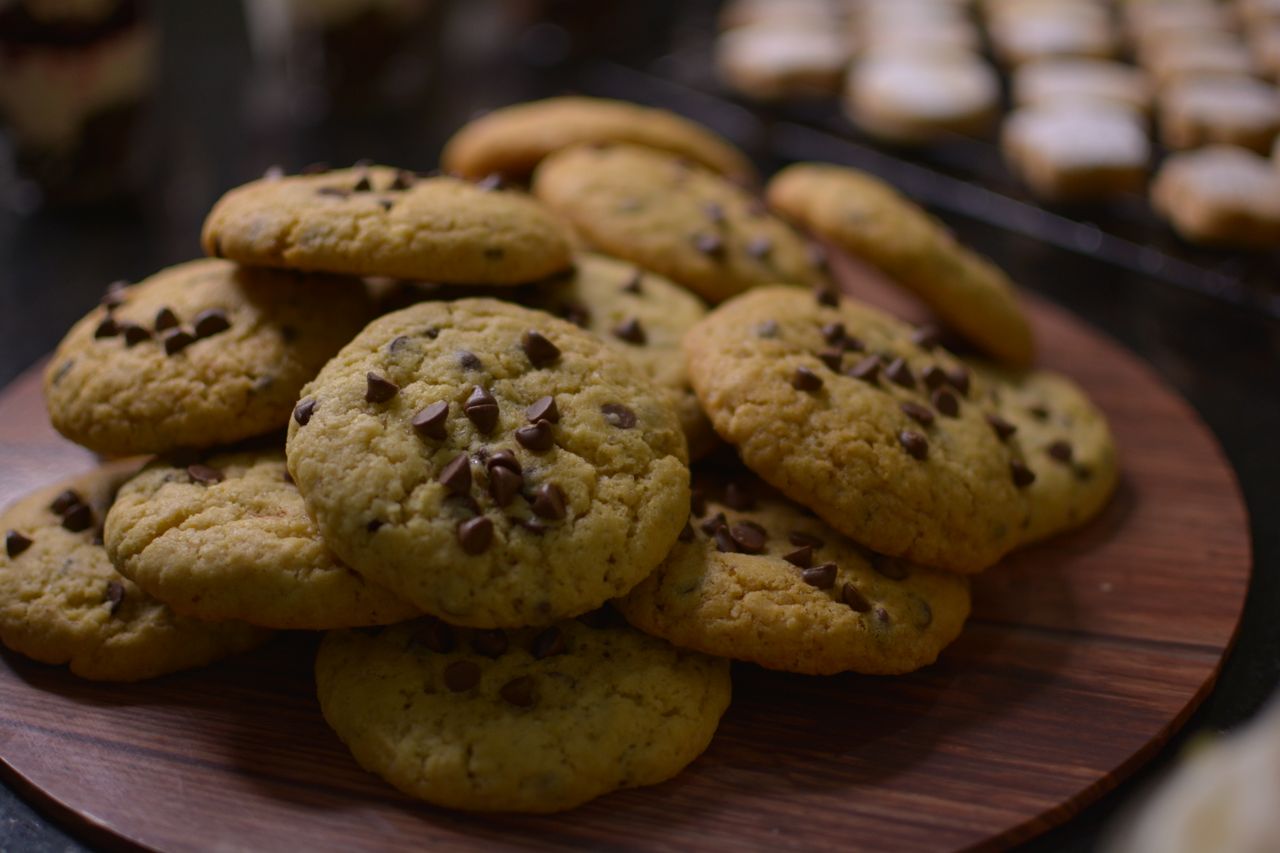 hero-img-02 Close-up view of freshly baked chocolate chip cookies on a wooden tray.
