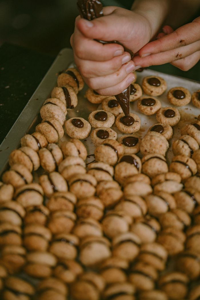 services-02 Close-up of hands preparing chocolate-filled cookies on a baking tray.